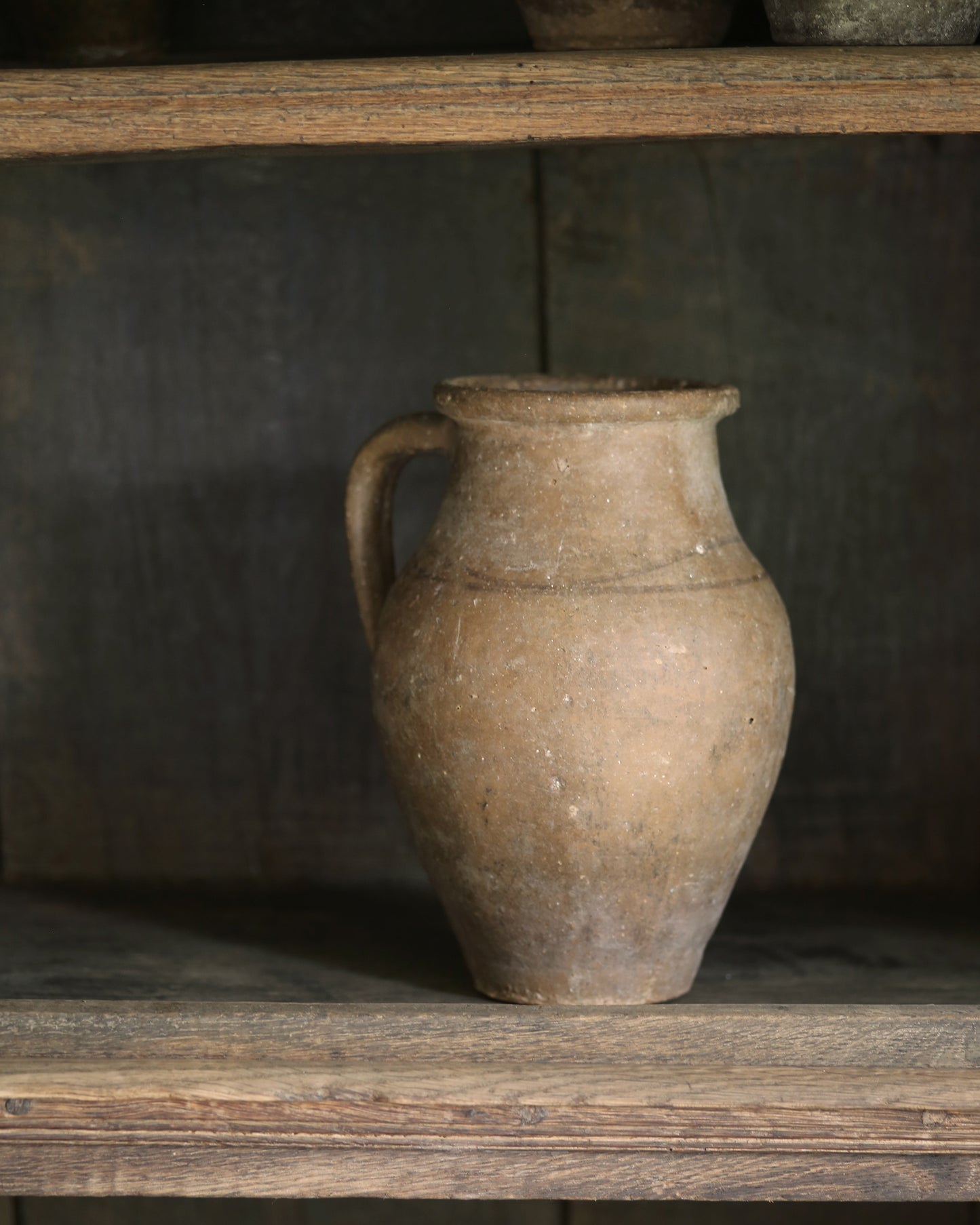 Brown ceramic pitcher pot on a wooden shelf with a dark background