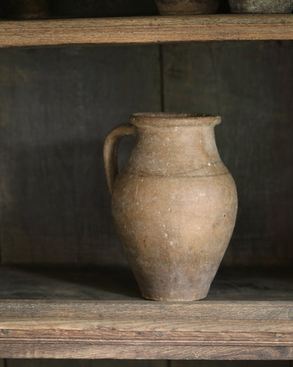 Brown ceramic pitcher pot on a wooden shelf with a dark background