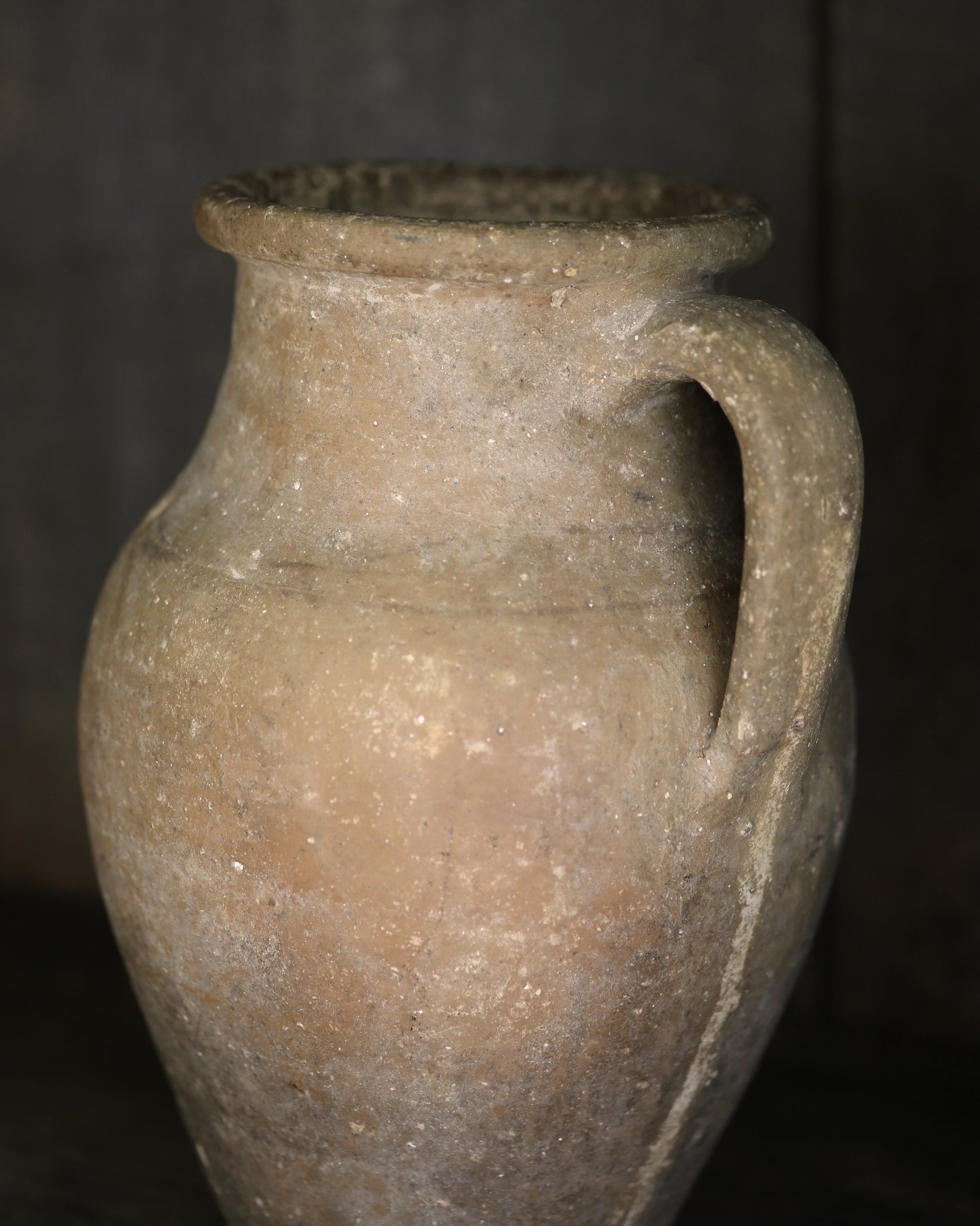 Ancient terracotta jar with a handle on a dark background