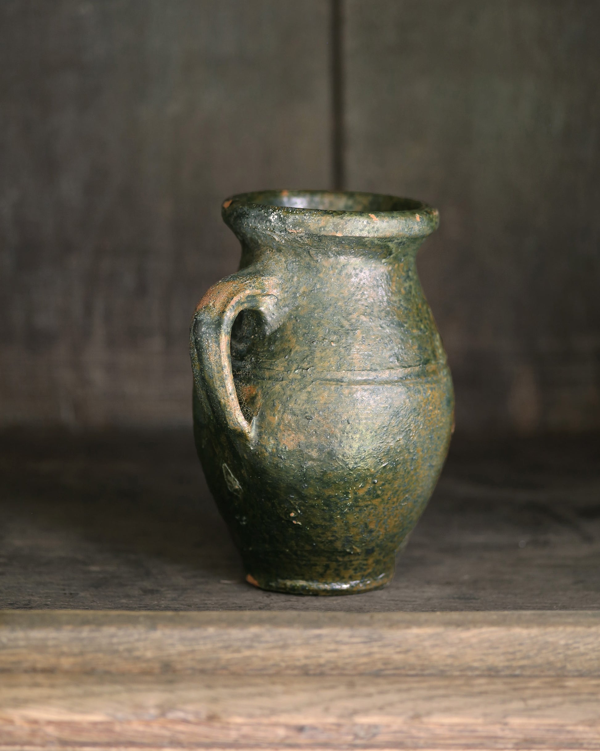 Green ceramic jar with a handle on a wooden surface with a dark background