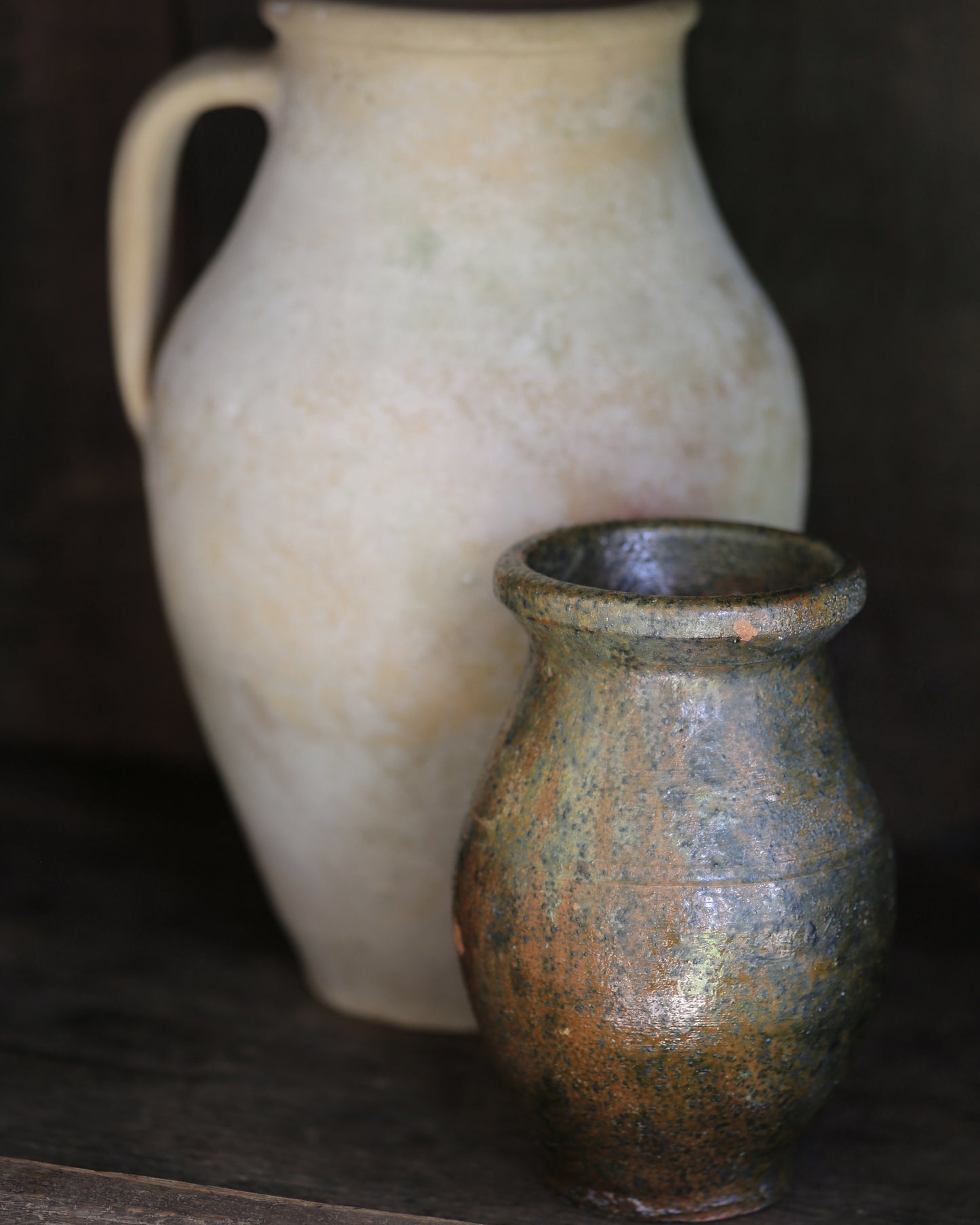 Two ceramic vases, one large and white, the other small and brown, on a dark shelf.
