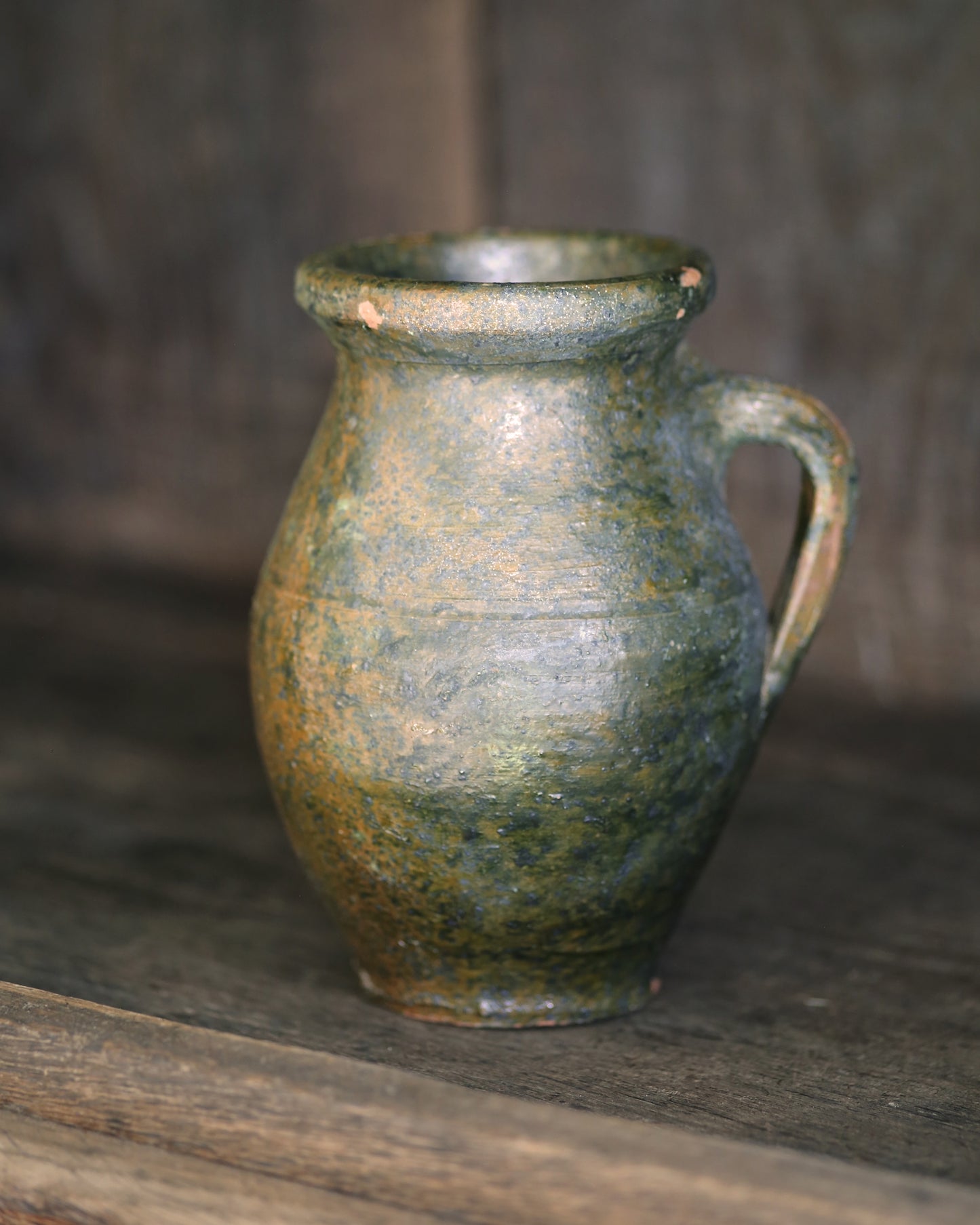 Green glazed ceramic pitcher on a wooden surface with a blurred background