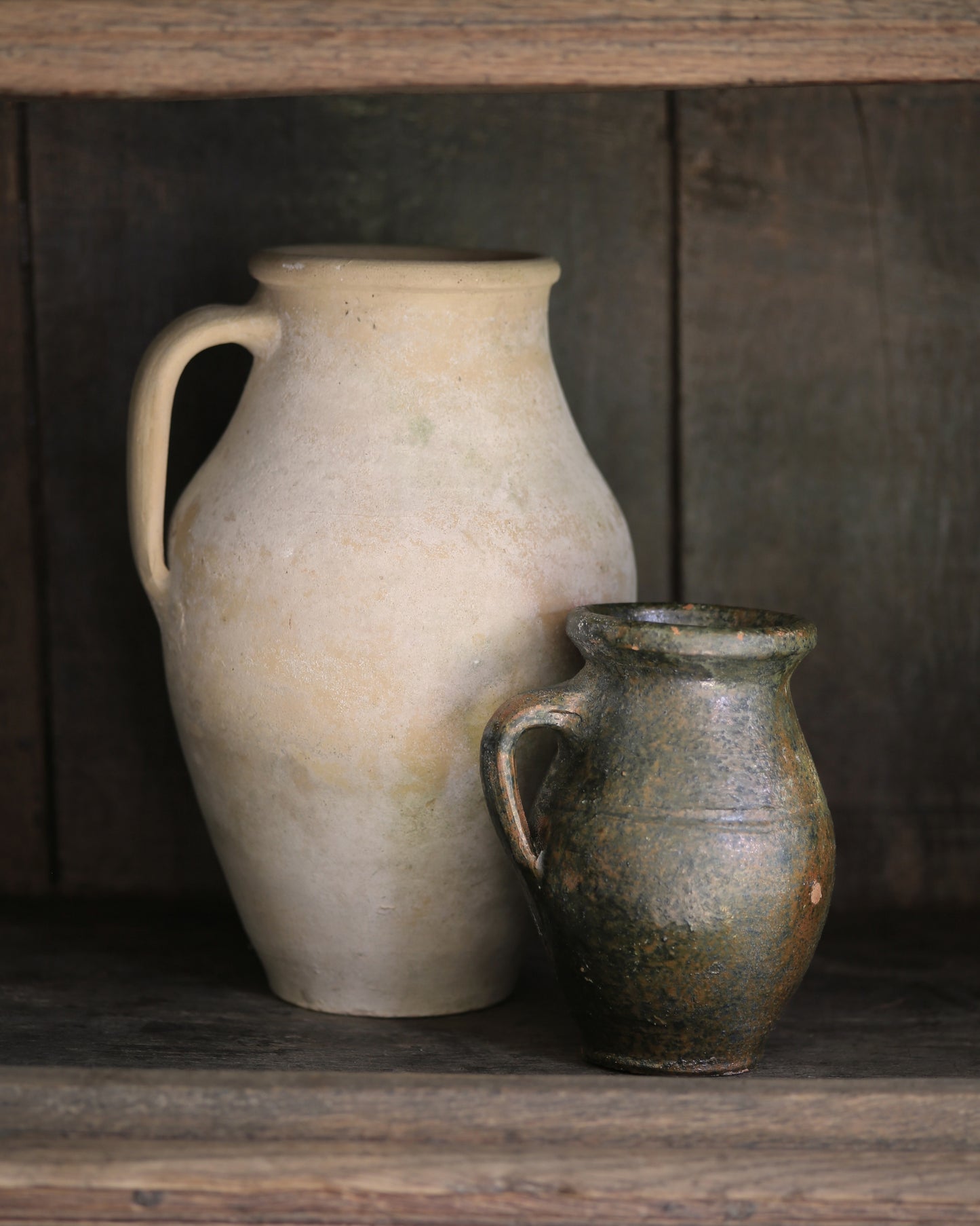 Two ceramic jars on a wooden shelf with a dark wooden panel background