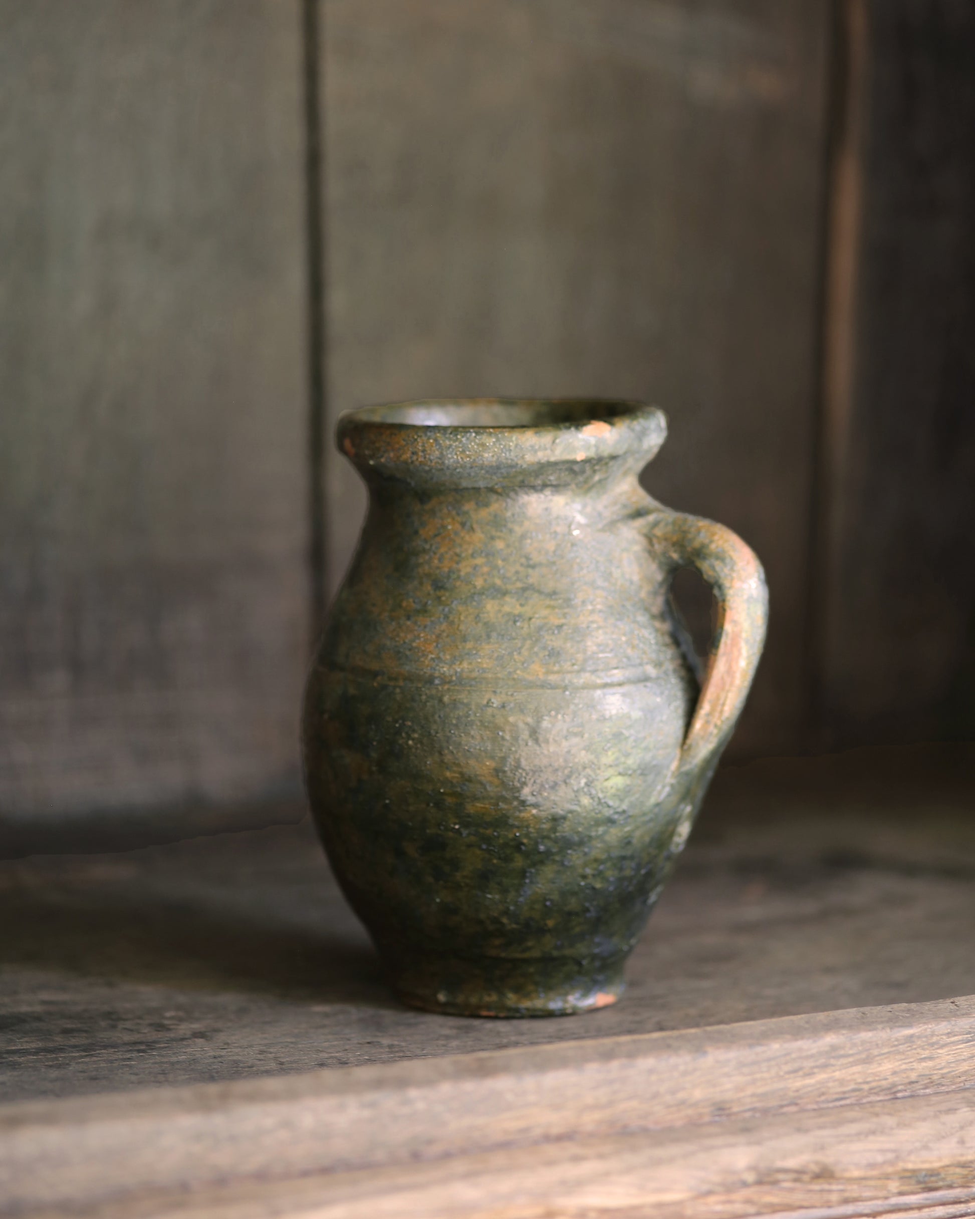 Small vintage green glazed ceramic pitcher on a wooden shelf