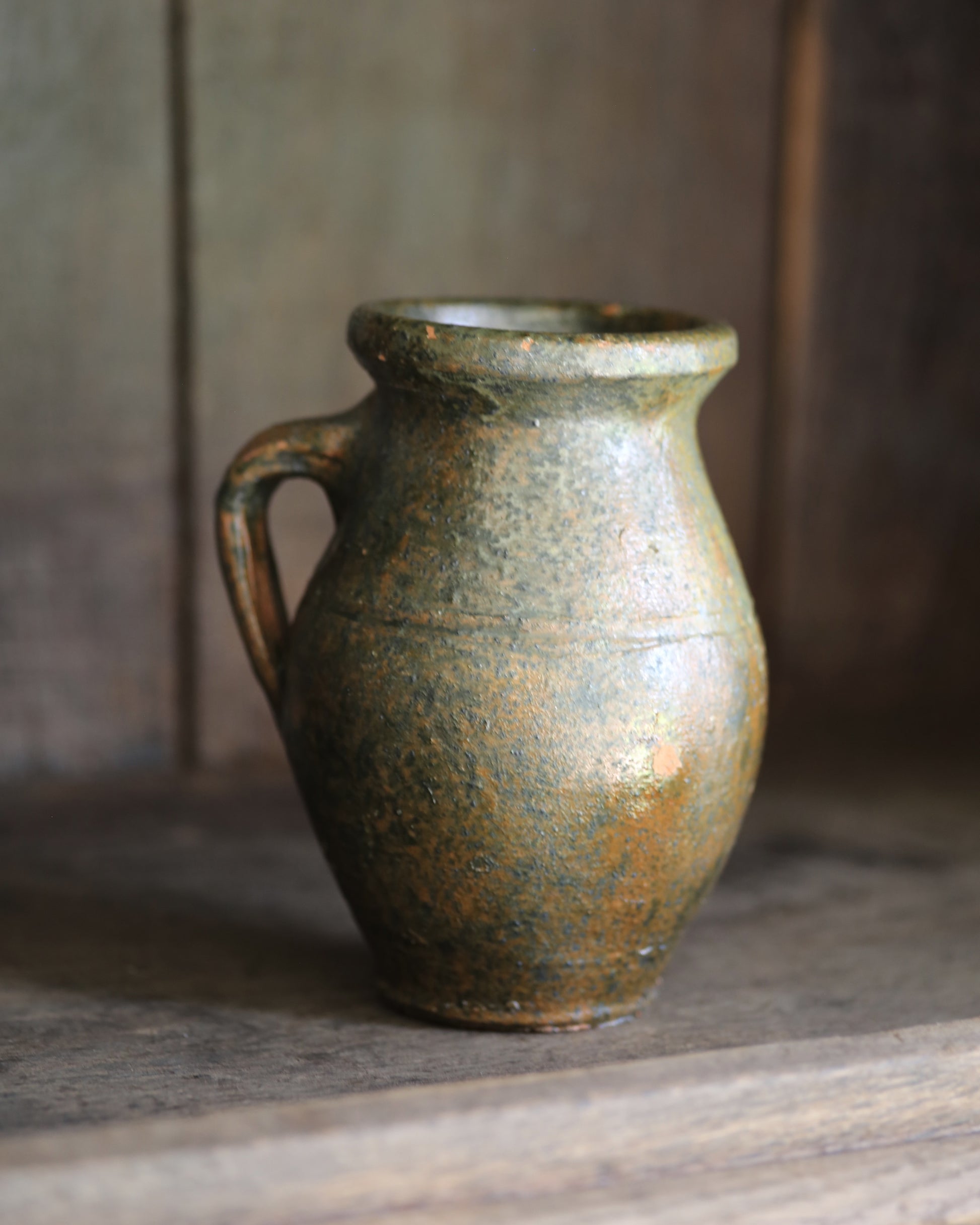 Vintage green glaze small pitcher pot on wooden shelving.