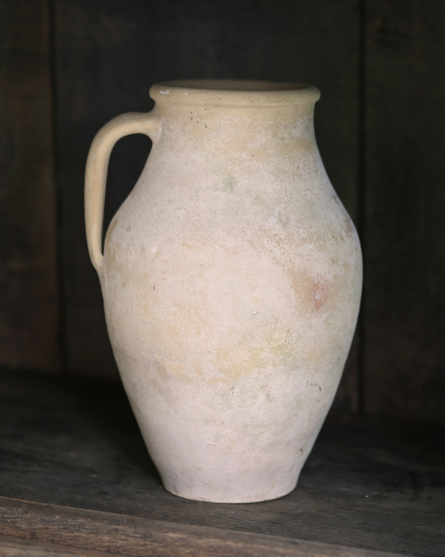 Whitewash pale sand coloured clay pitcher pot on a dark wooden surface with a dark background
