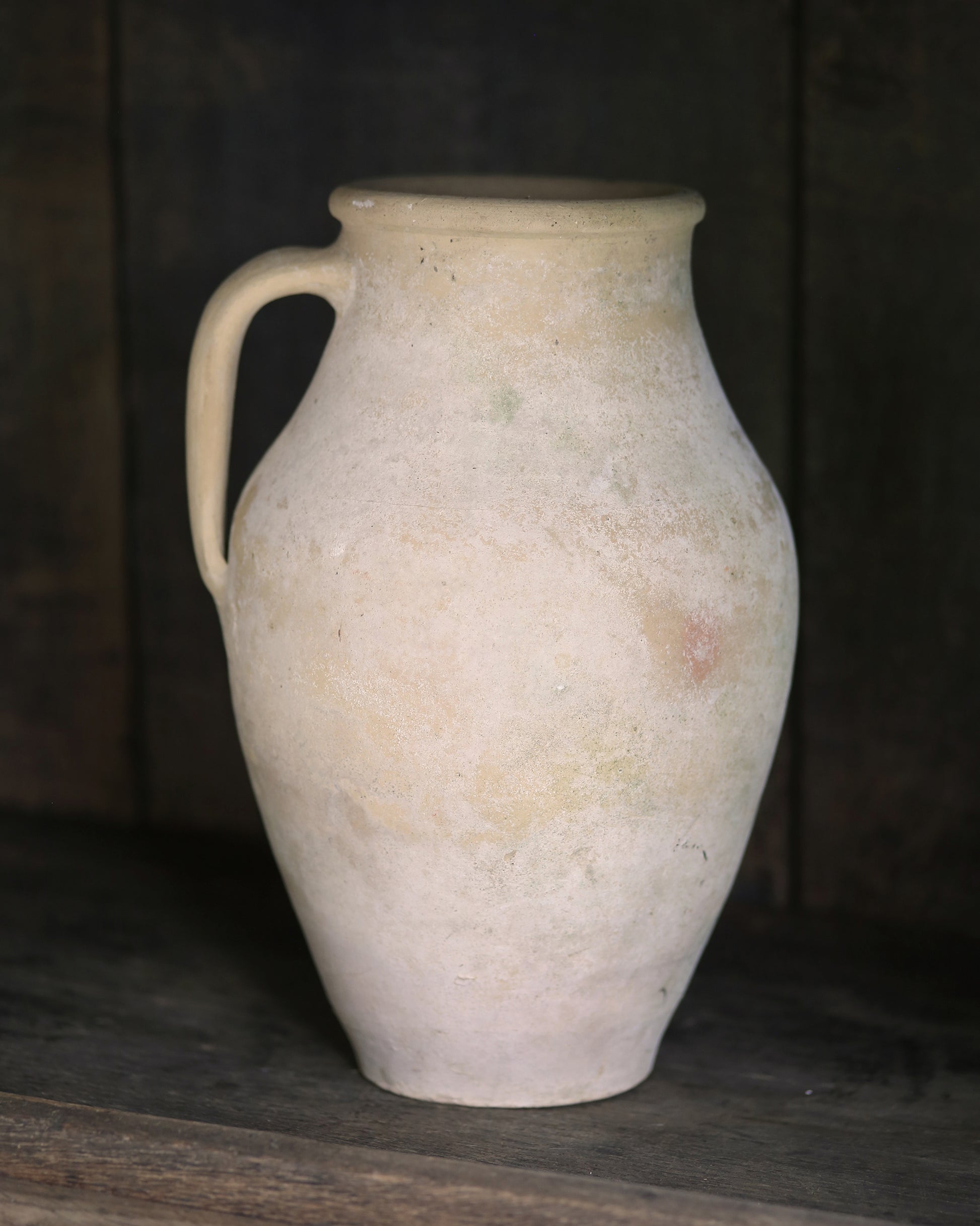Whitewash pale sand coloured clay pitcher pot on a dark wooden surface with a dark background
