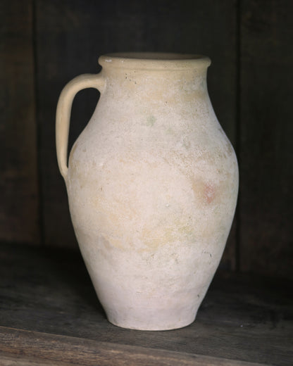 Whitewash pale sand coloured clay pitcher pot on a dark wooden surface with a dark background