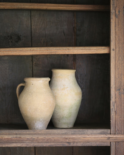 Two rustic vintage clay vases on a wooden shelf against a dark wooden panelled bookcase.