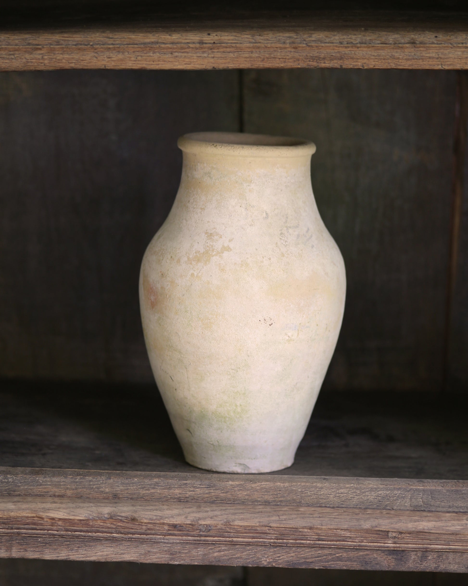 White ceramic vase on a wooden shelf with a dark background