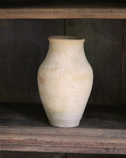 White ceramic vase on a wooden shelf with a dark background
