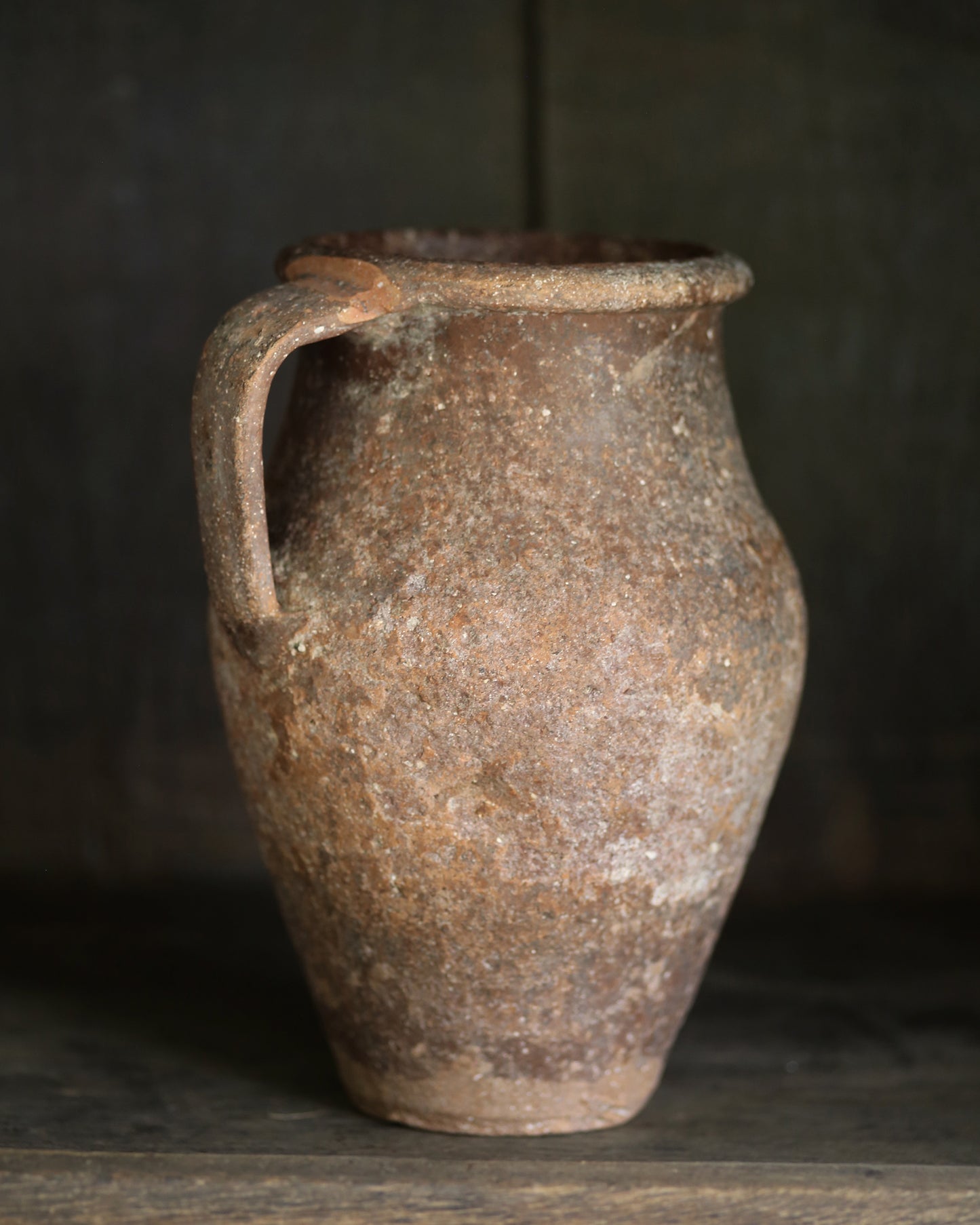 Brown ceramic pitcher pot with rustic texture on a dark background