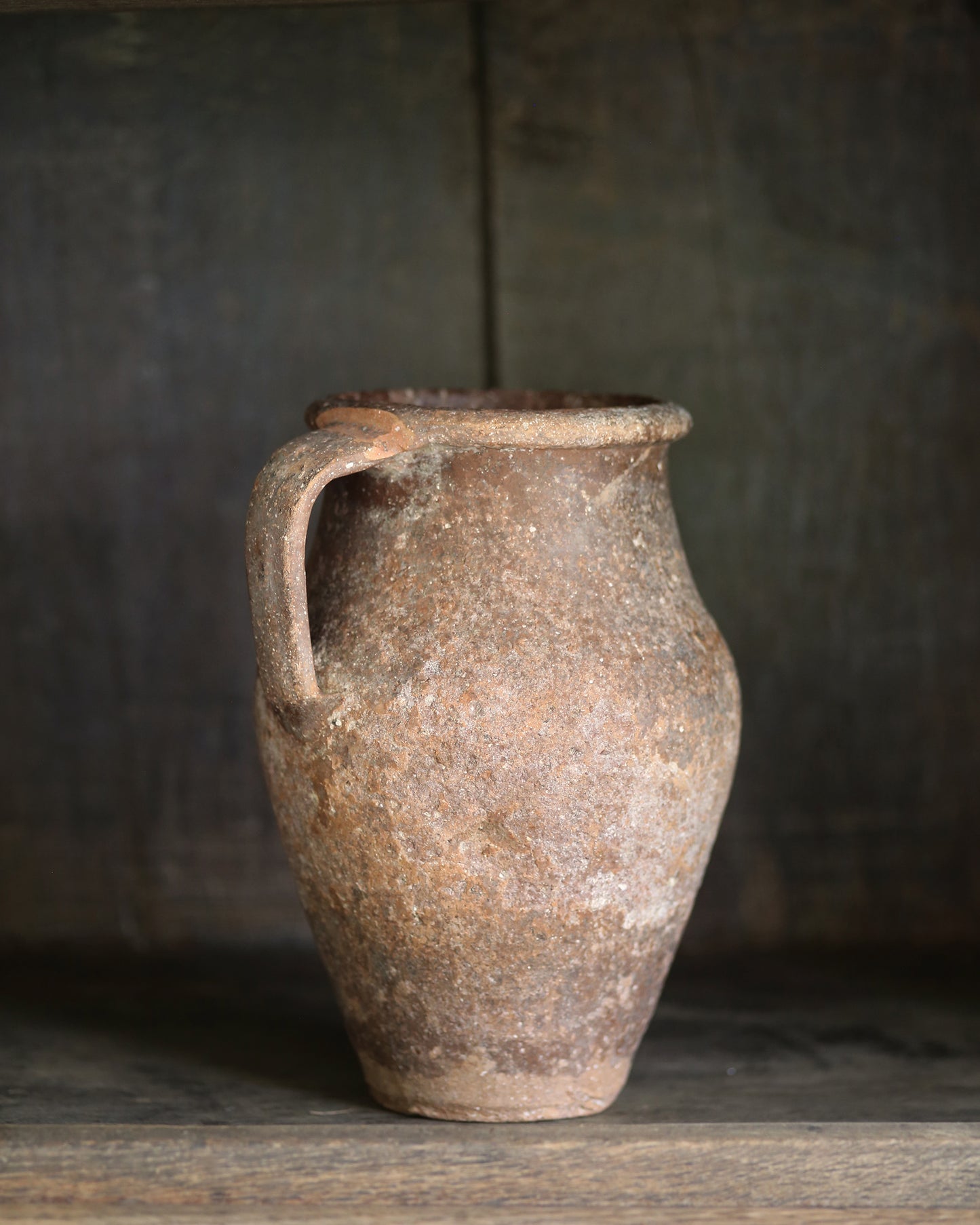 Vintage terracotta jar with a handle on a wooden surface against a dark background
