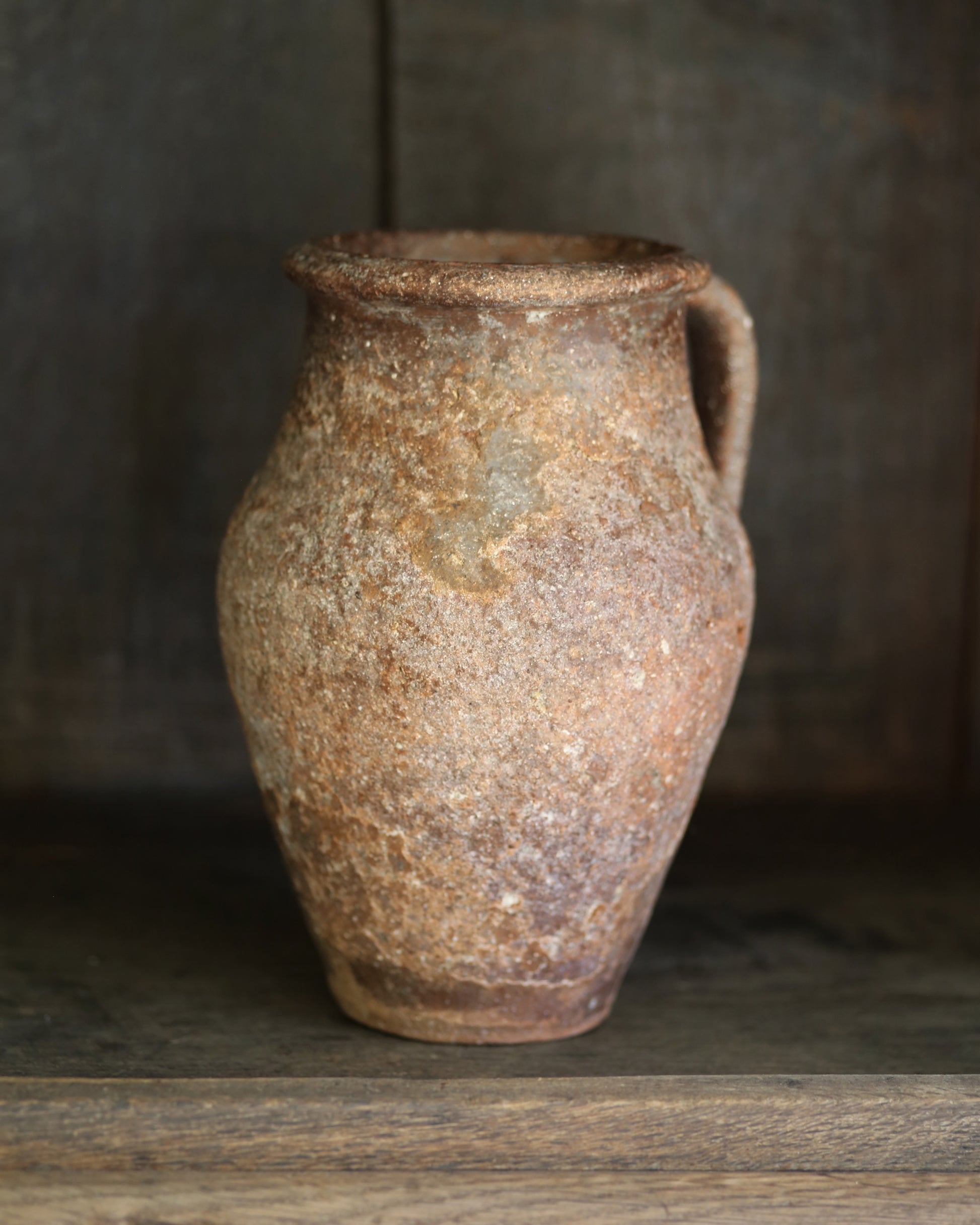 Rustic brown clay pitcher pot on a wooden surface with a dark background