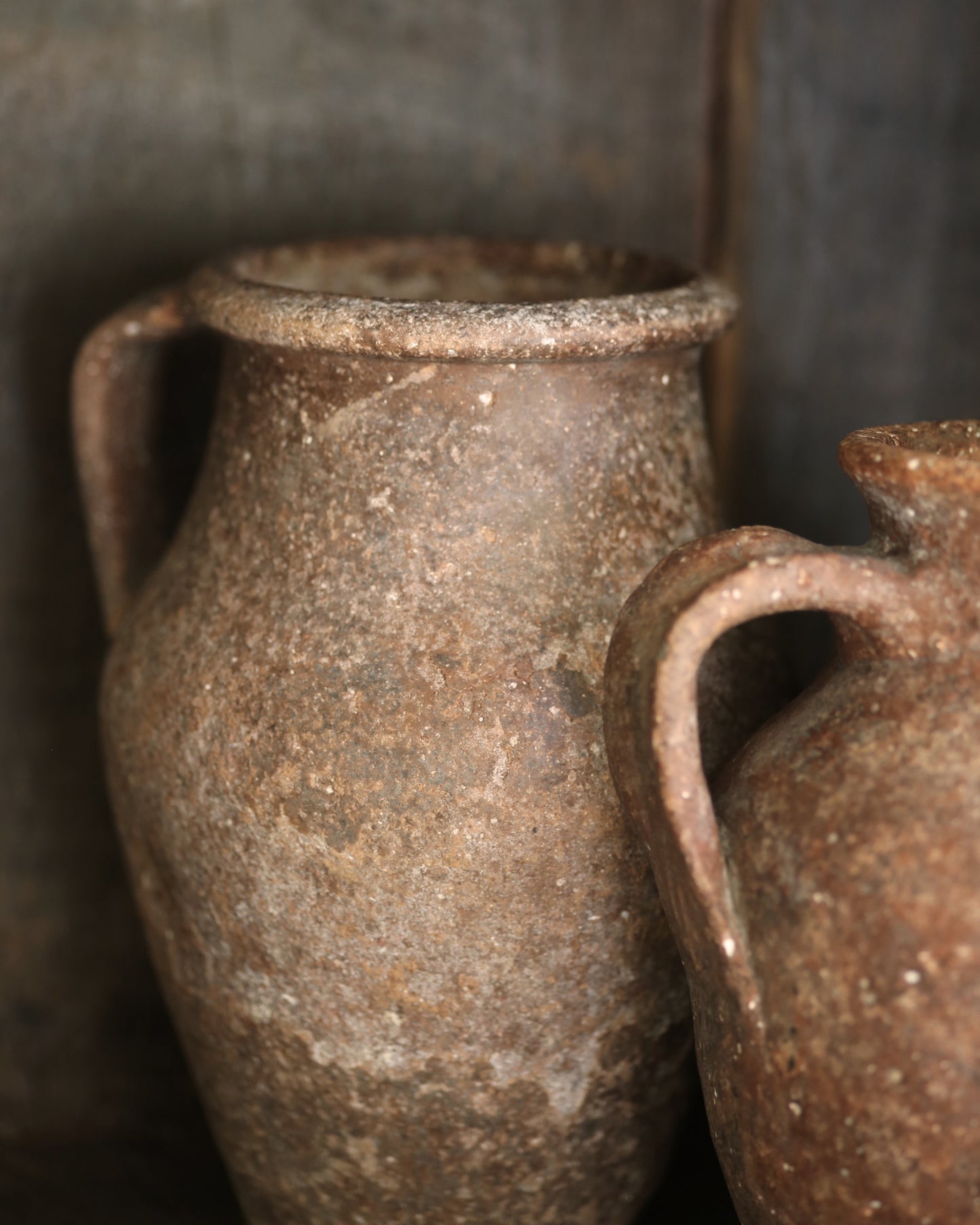 Two rustic brown ceramic jars with handles against a dark background