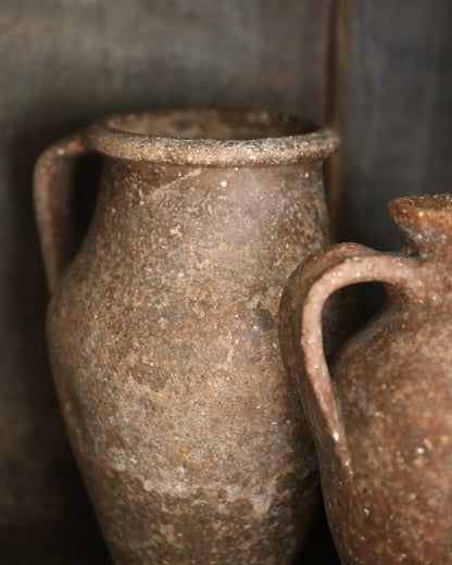 Two rustic brown ceramic jars with handles against a dark background