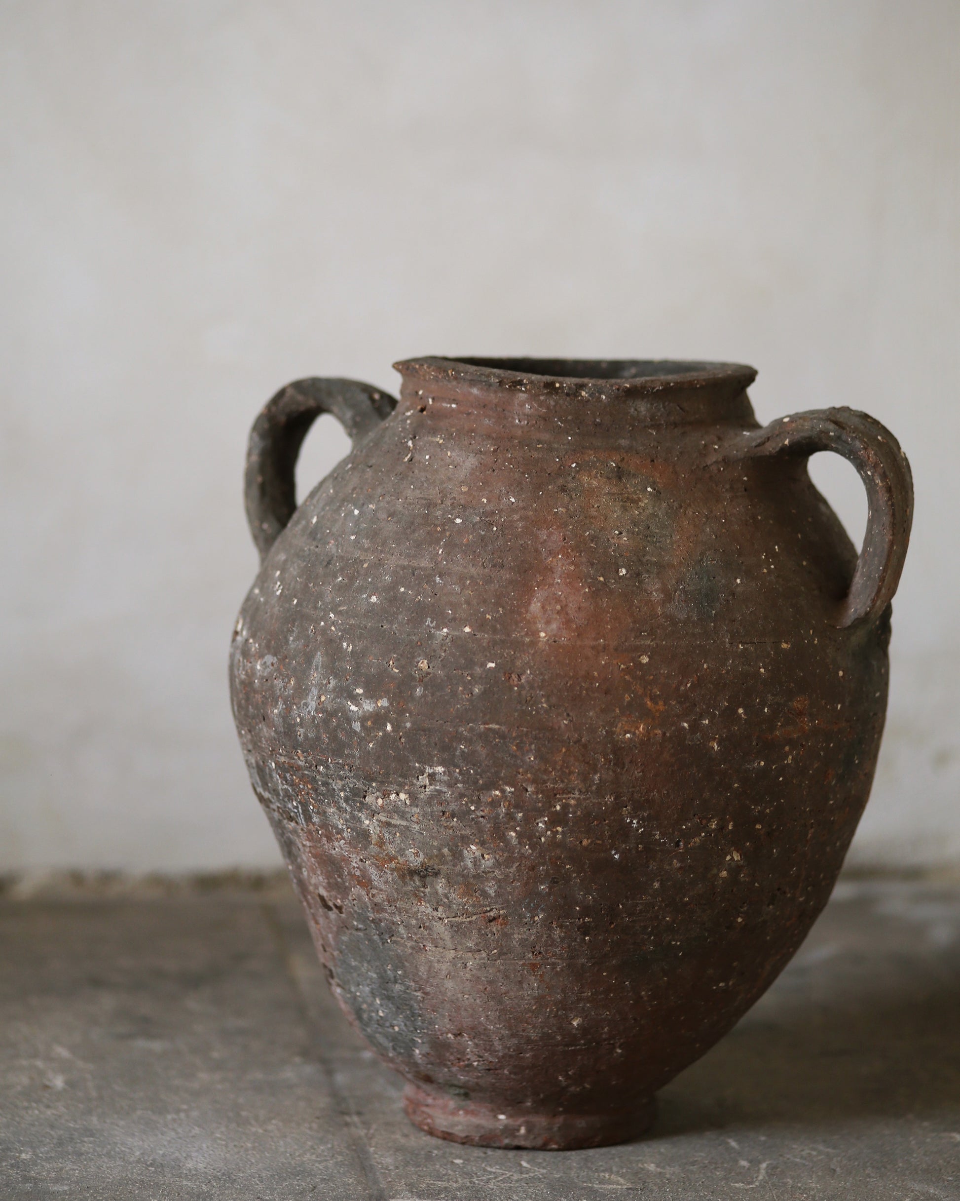 Old antique rustic brown ceramic jar with two handles on a gray surface against a plain background