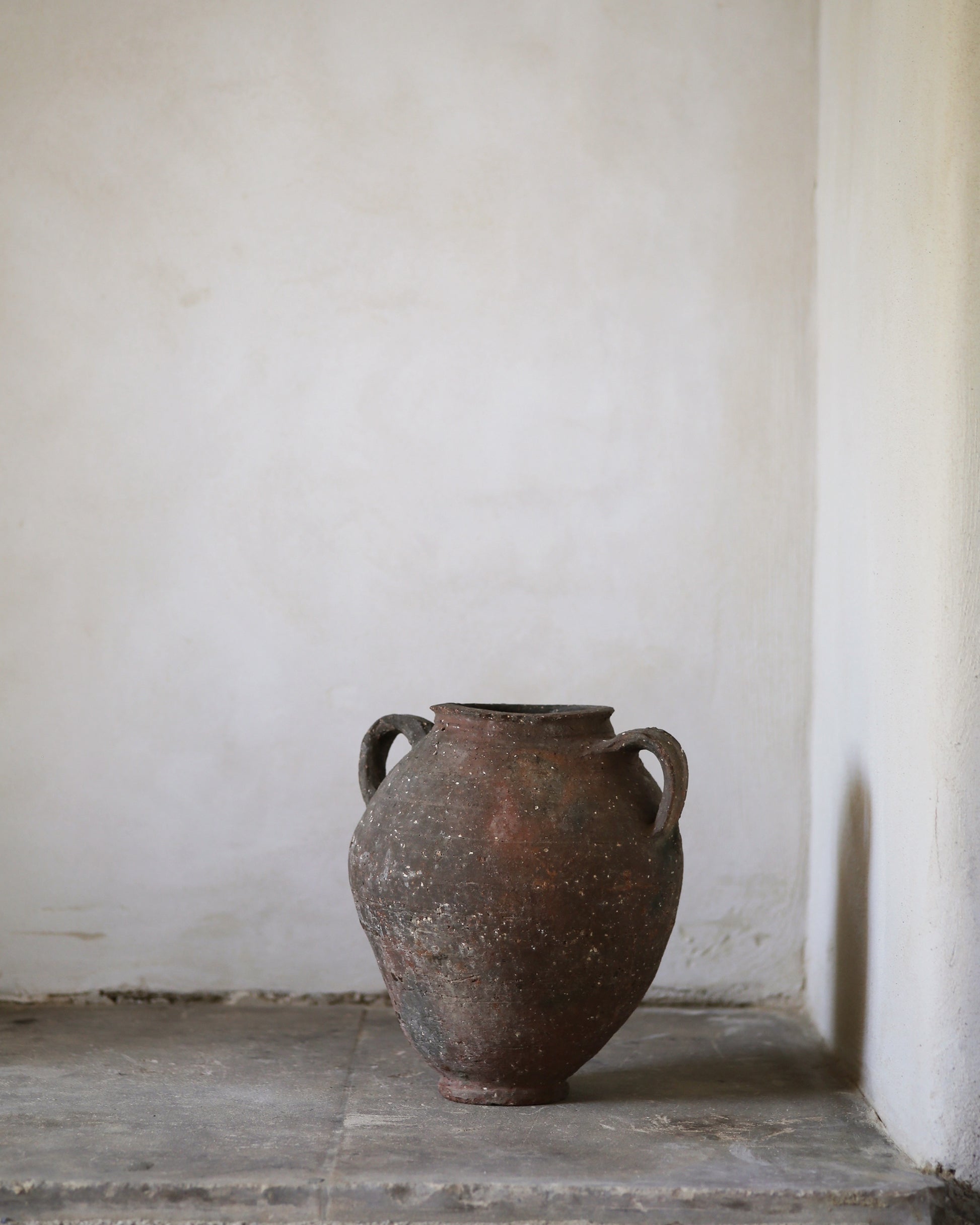 Vintage terracotta pottery on a stone surface with a white wall background
