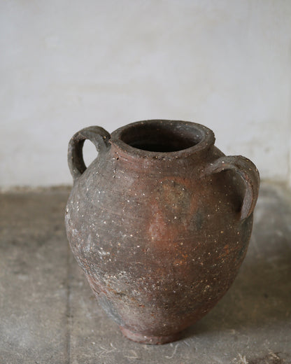 Ancient terracotta jar with two handles on a concrete floor.