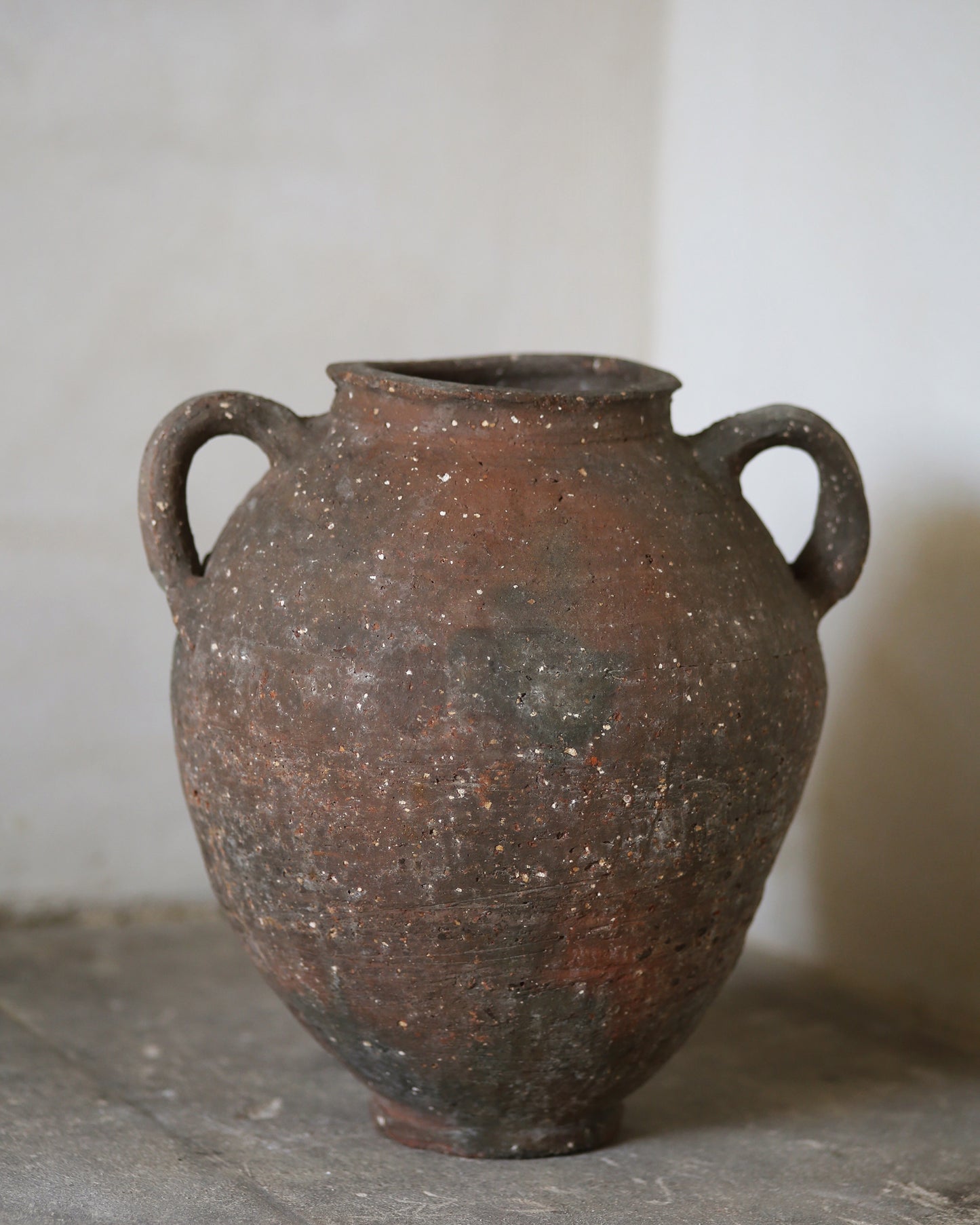 Brown clay jar with two handles on a gray surface.