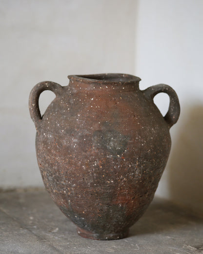 Brown clay jar with two handles on a gray surface.