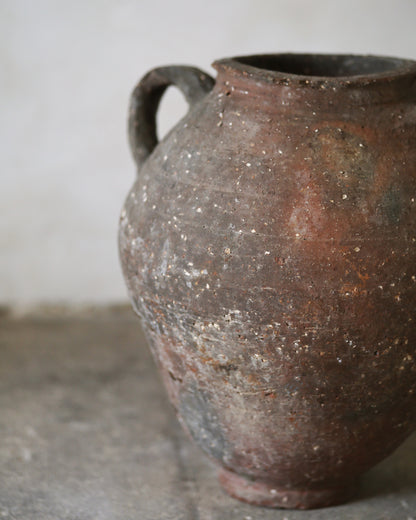 Brown ceramic urn with a handle sat on a gray flagstones