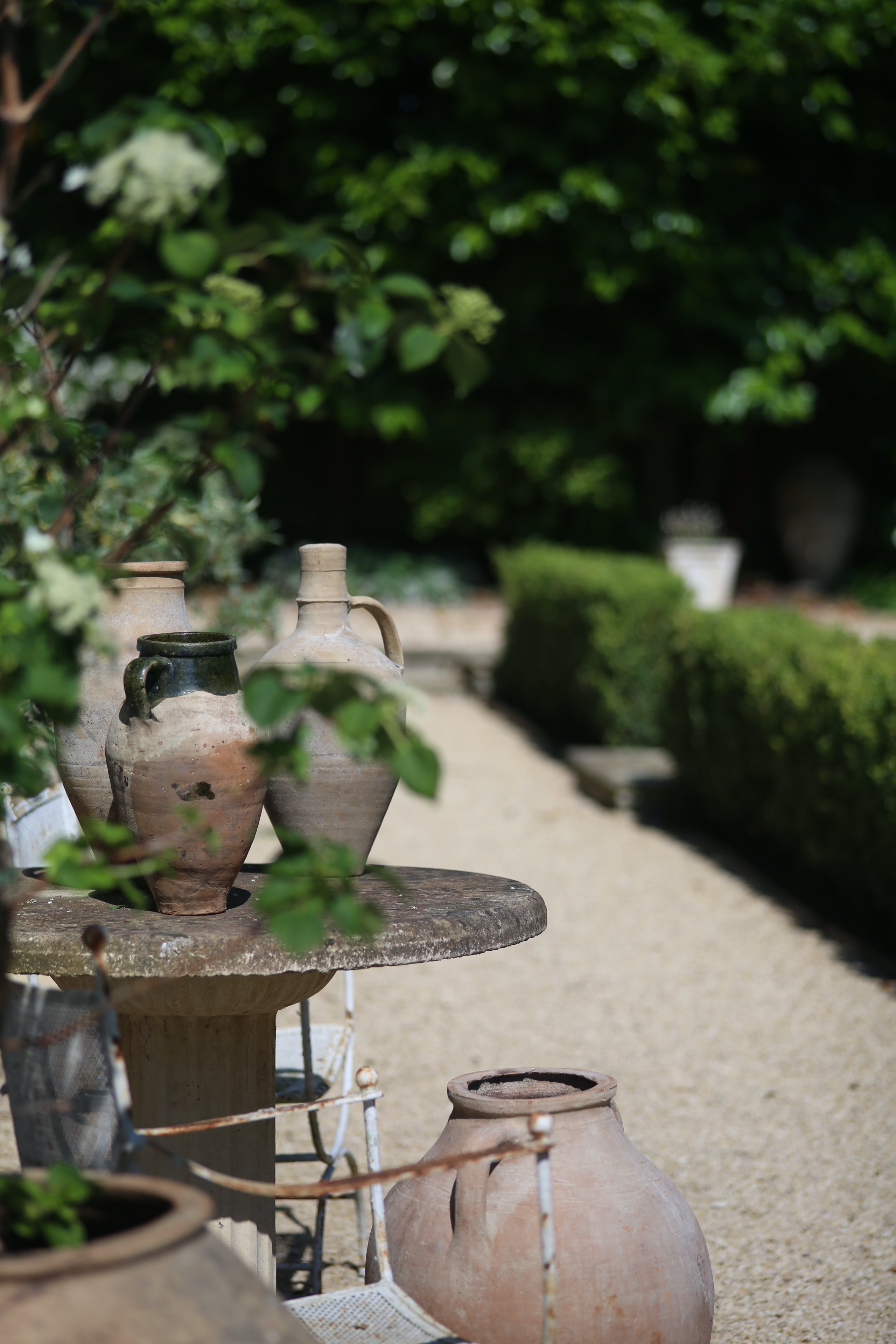 Small pottery pieces on antique french garden furniture + large planted olive pots on country garden path