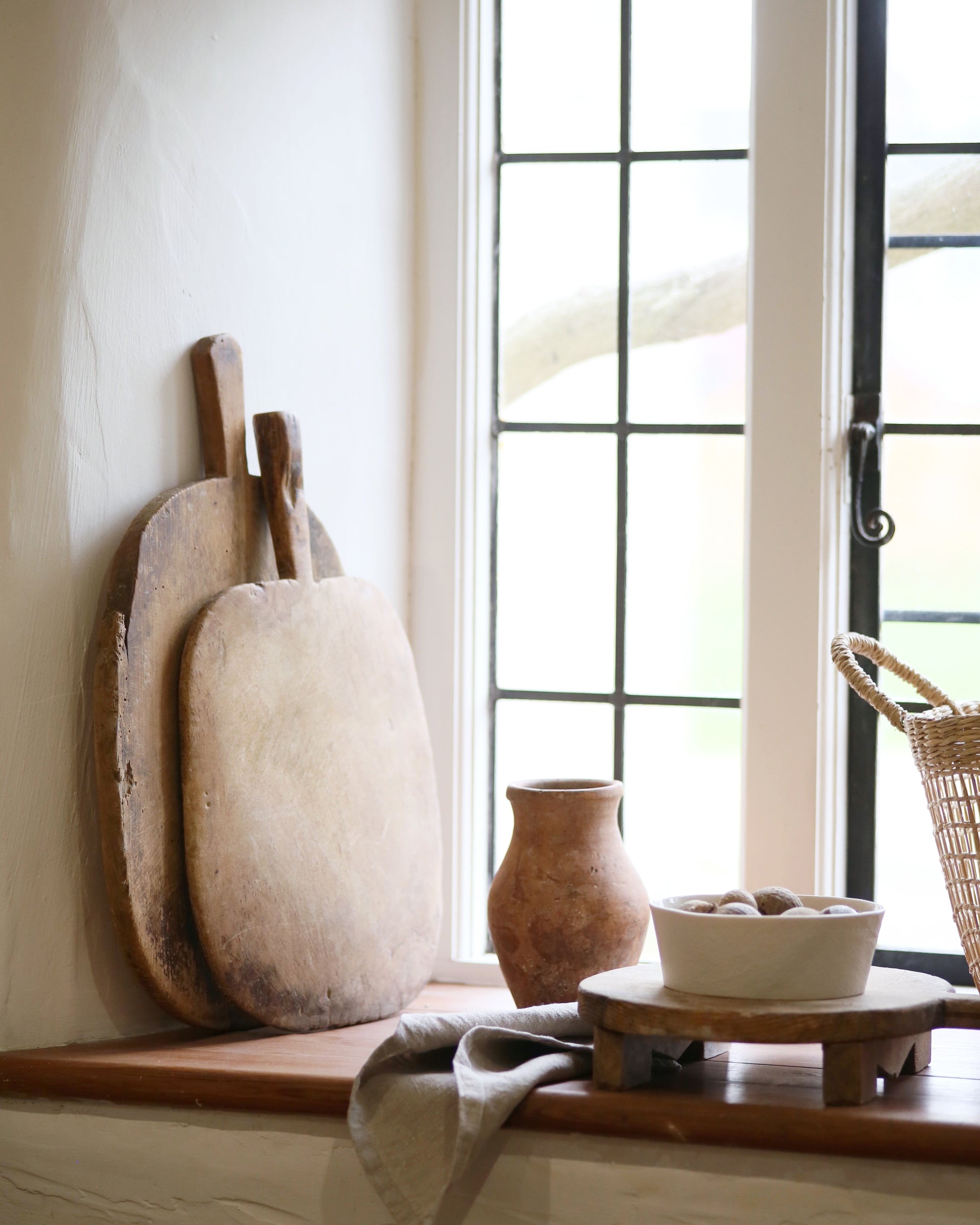 Kitchen window sill displayed with stacked antique chopping boards and pots